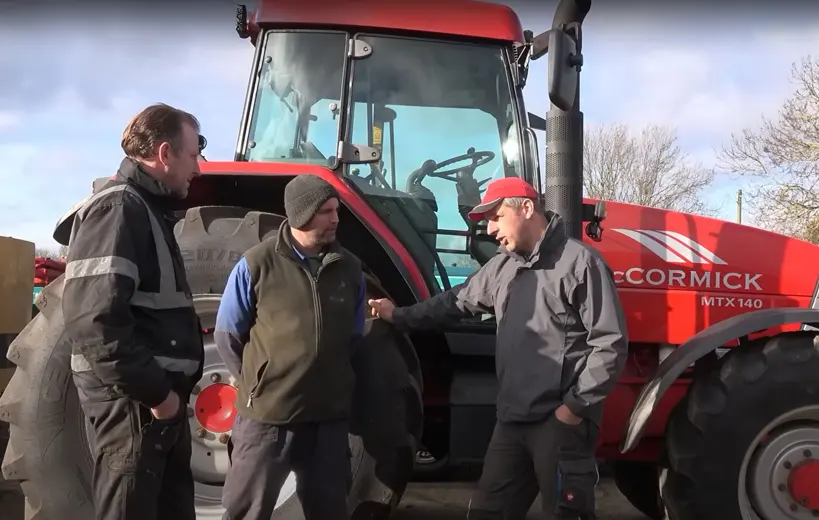 Three farmers talking next to a tractor